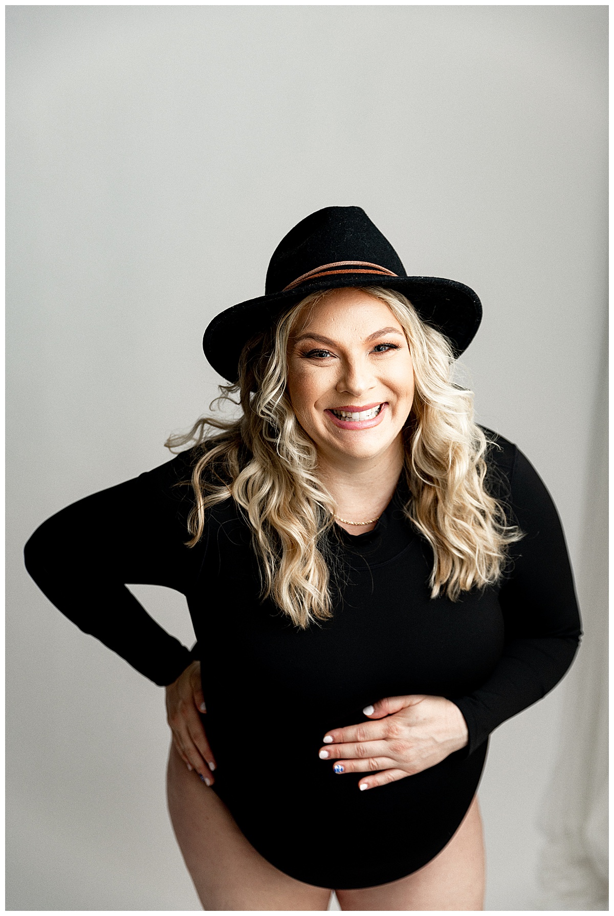 Woman wears black hat and outfit for IVF Maternity Session.