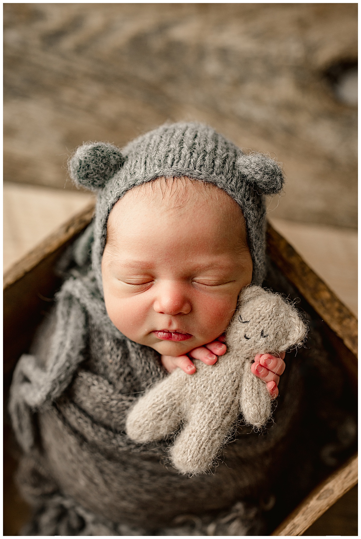 Infant in gray wrap holds bear for Norma Fayak Photography