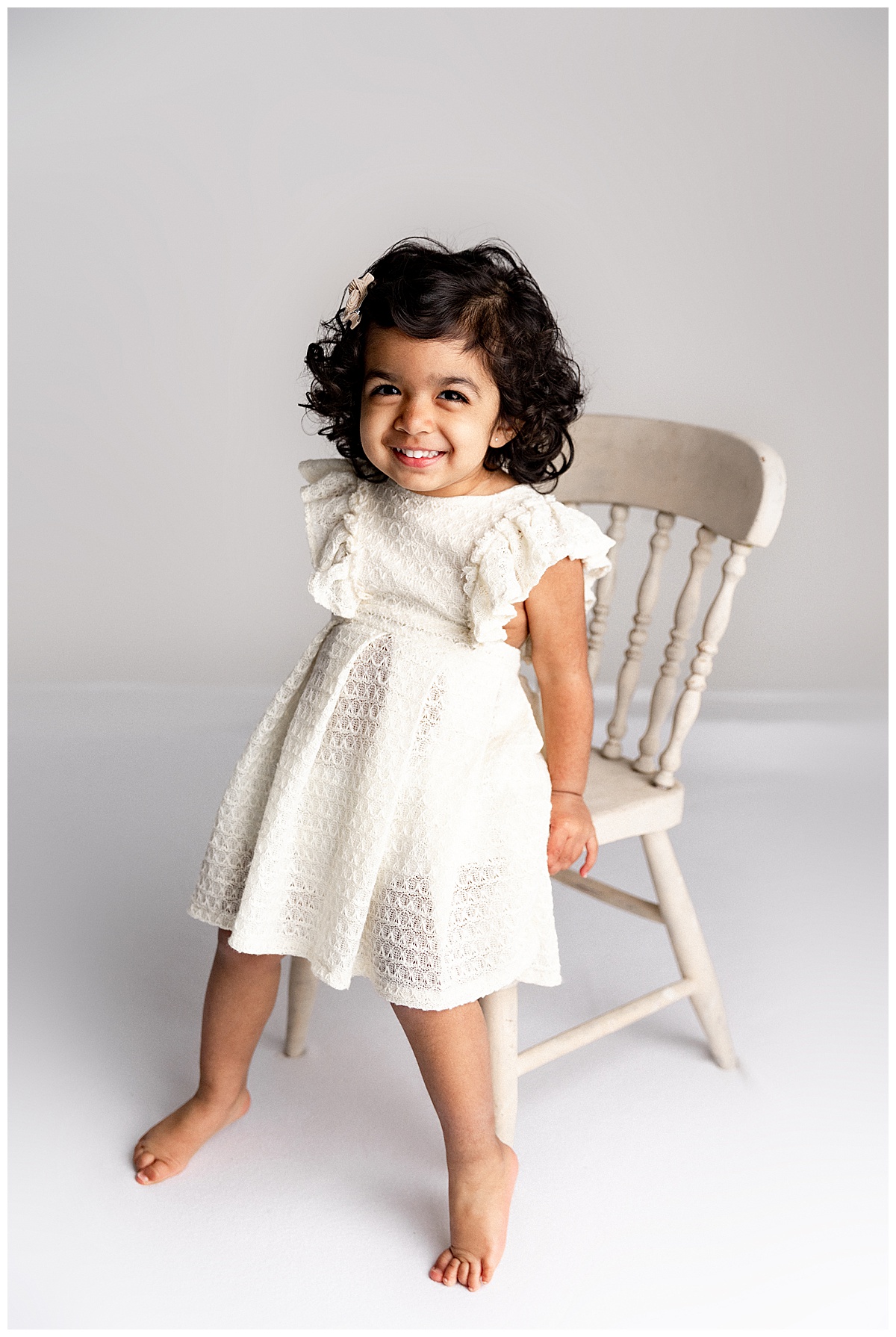 Baby girls sits on chair wearing white dress for Virginia Maternity Photographer