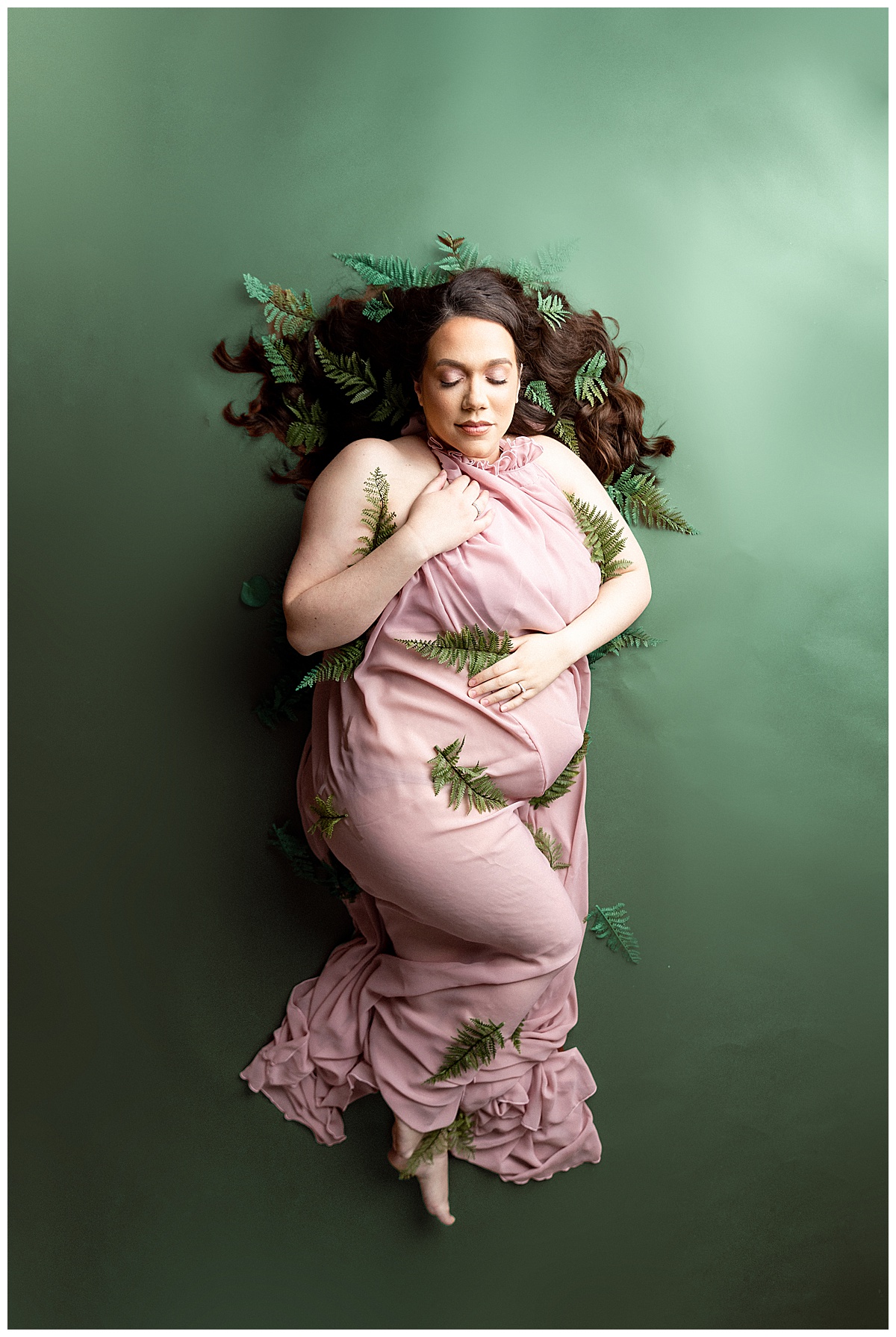 Mama holds gown to her body covered in greenery for Virginia Maternity Photographer