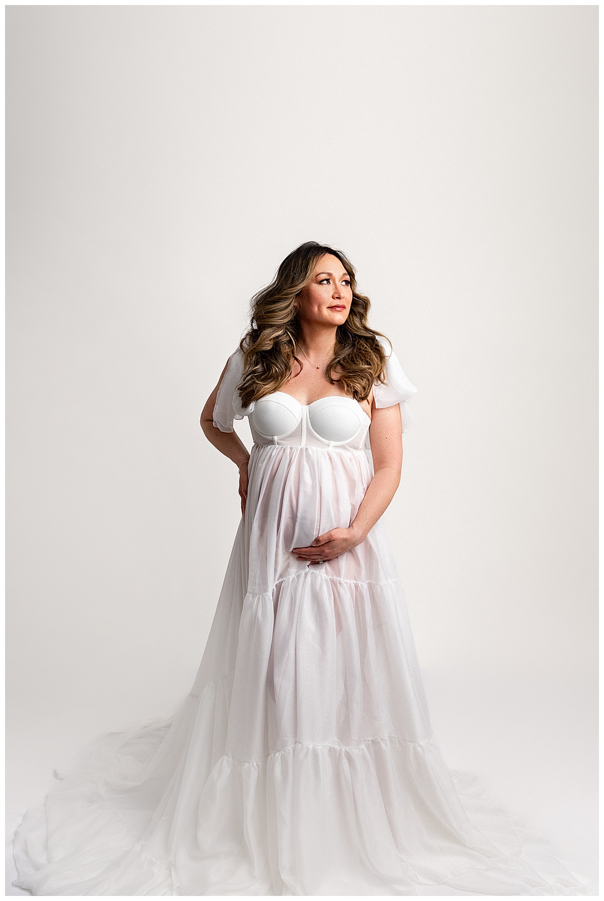 Mother holds pregnant belly wearing white maternity gown for Norma Fayak Photography 