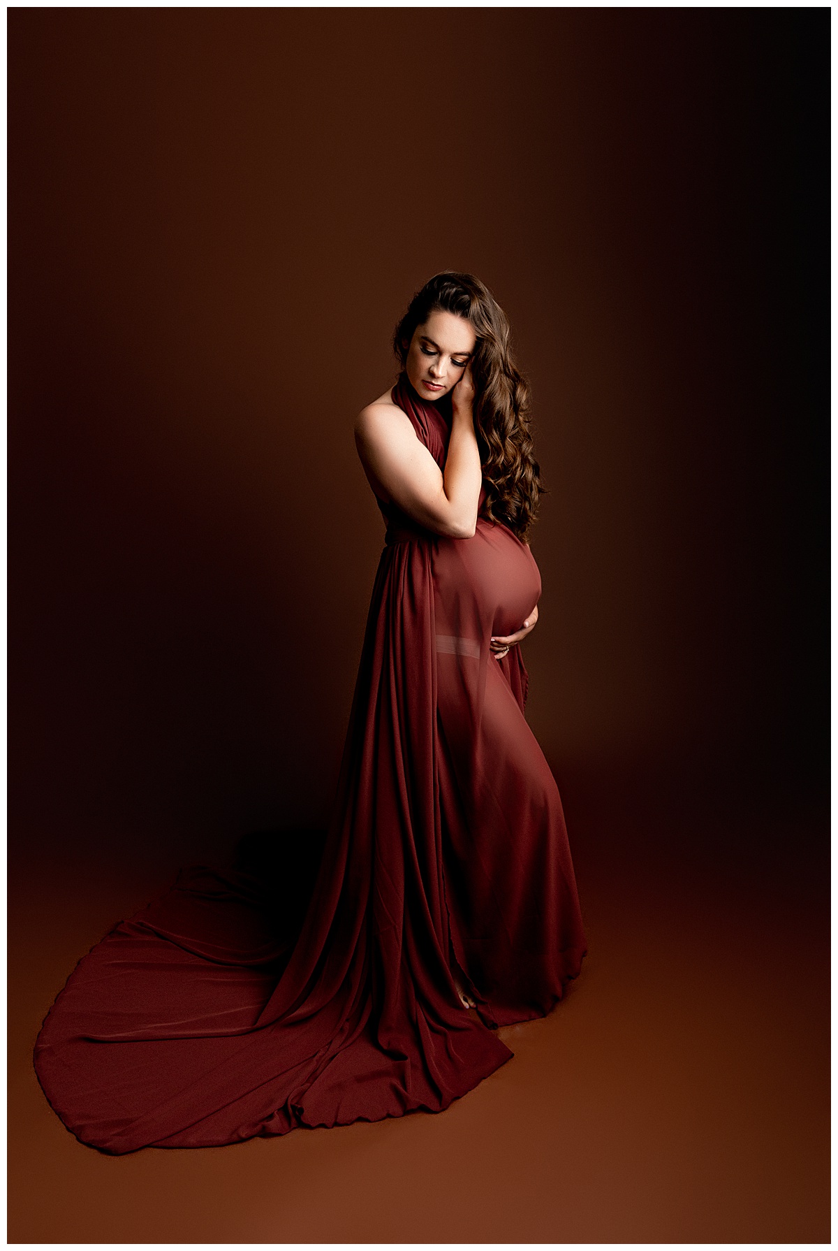 Woman wears gorgeous maroon dress and holds pregnant belly for Norma Fayak Photography