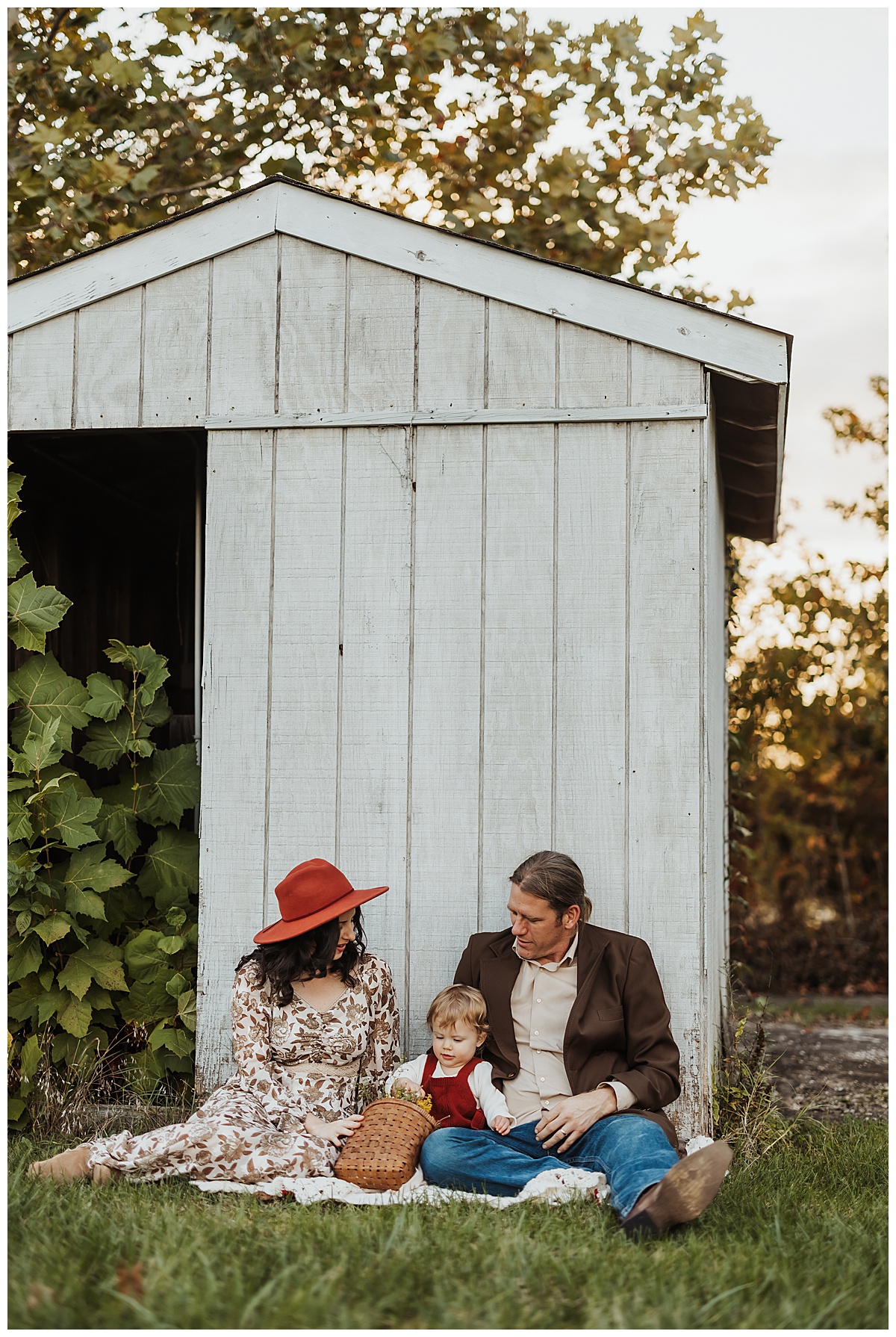 Family sits in front of white wooden barn during their Golden Hour Family Session
