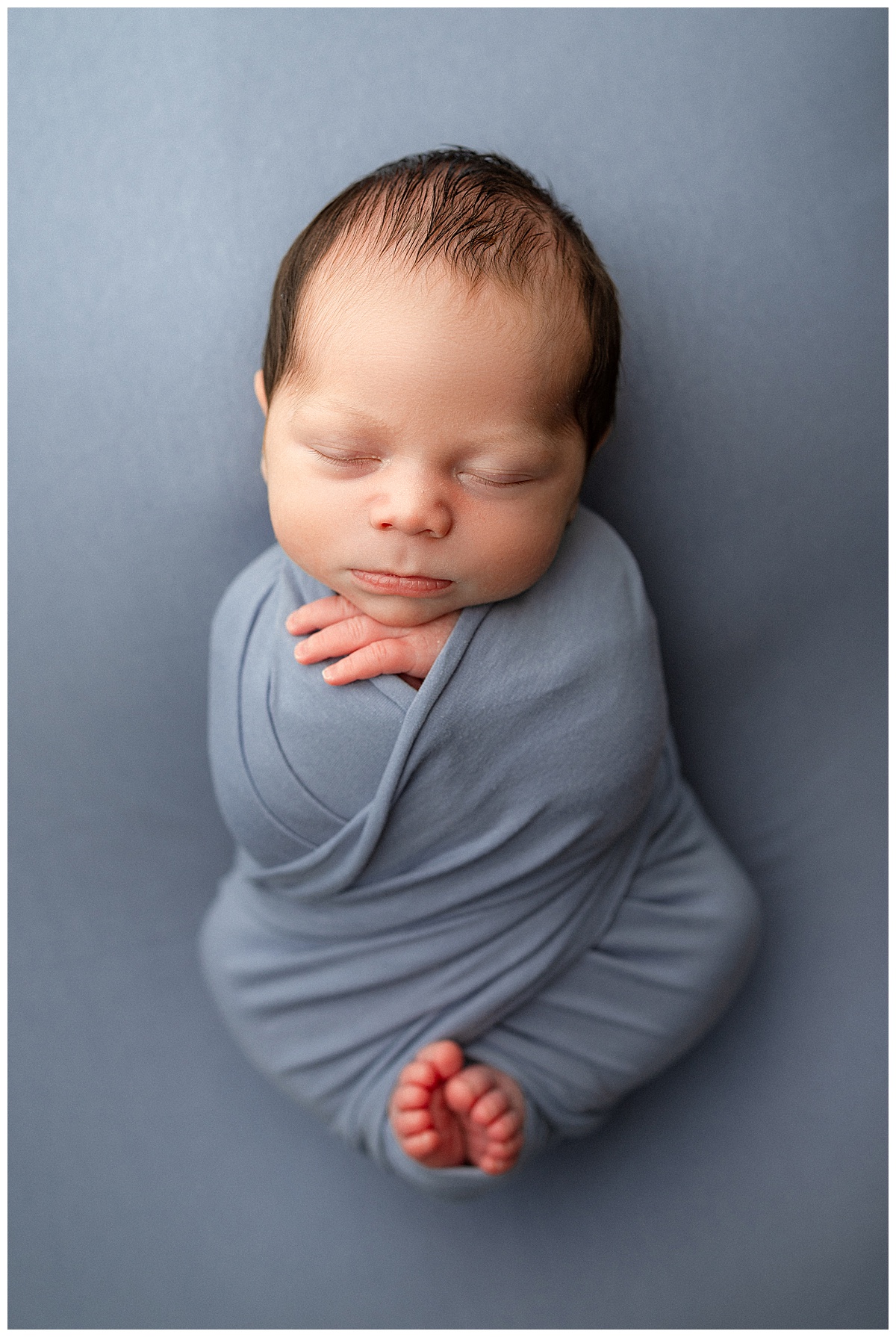 Baby lays wrapped tightly in blue wrap for Norma Fayak Photography