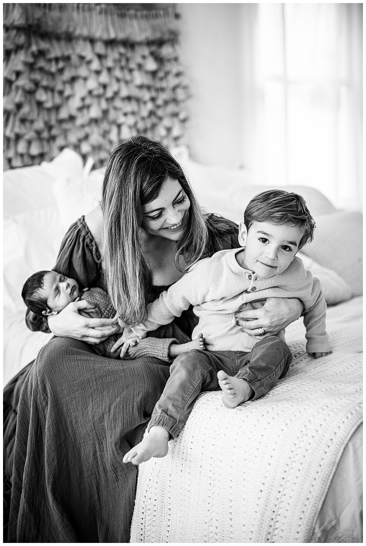 Mom sits on bed holding two kids for Norma Fayak Photography