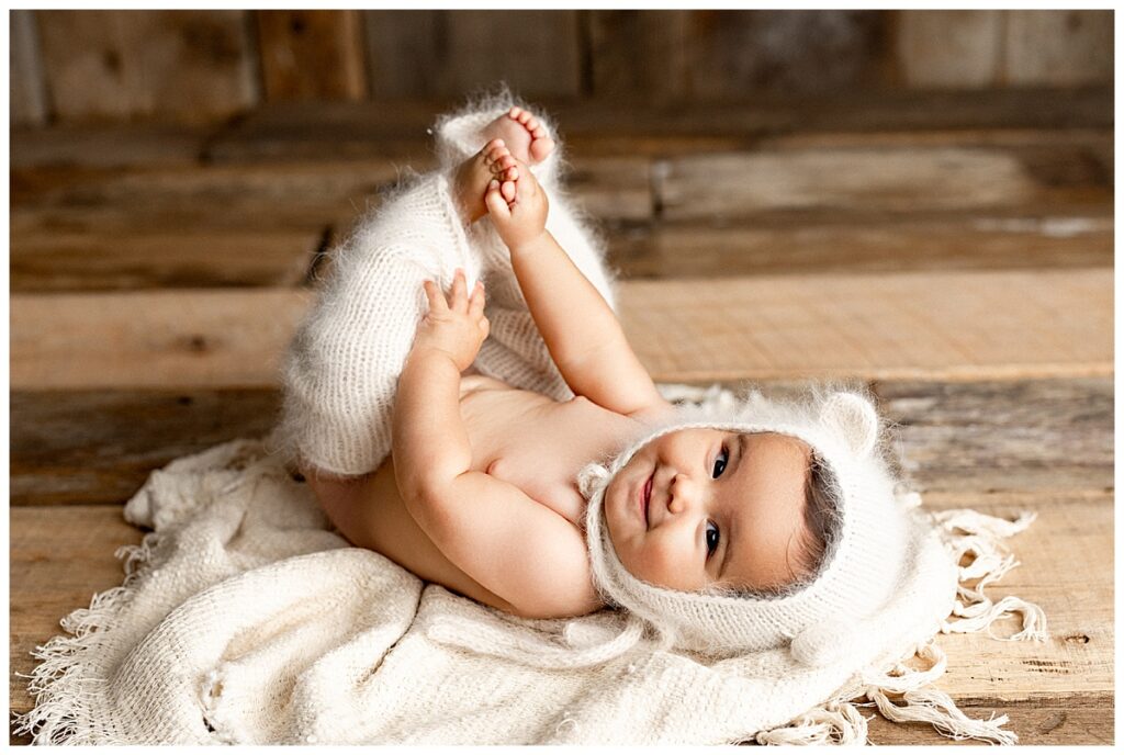 Baby lays on the ground holding feet in the air during her baby photography session