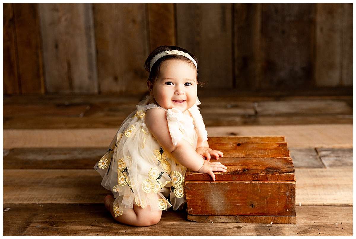 Baby kneels onto wooden box during 6-Month Sitter Session