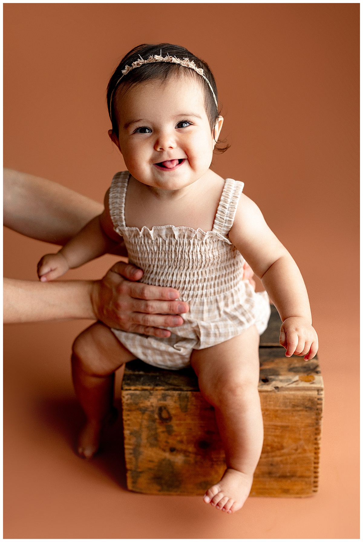 Young girl sits on wooden box during baby photography session