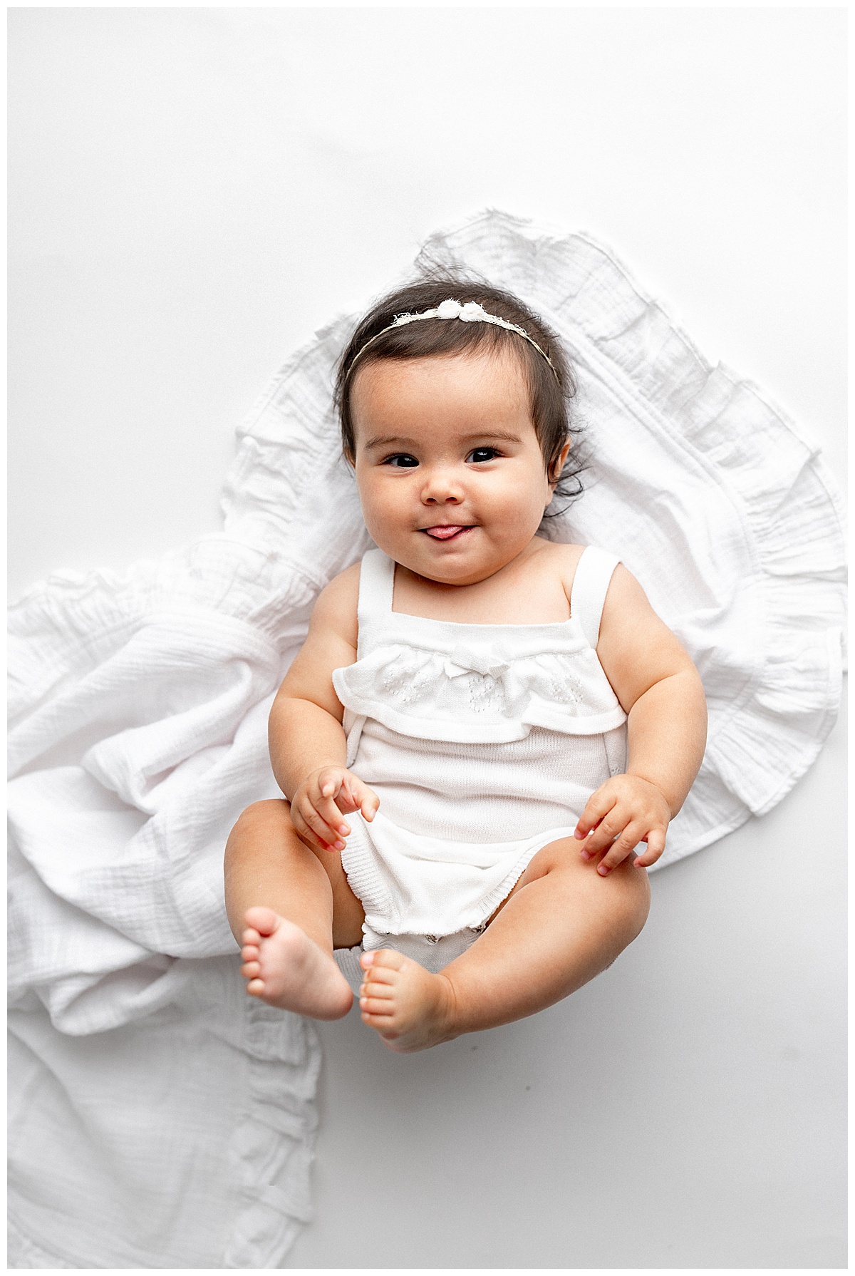 Baby lays on the ground in white outfit during baby photography sesson